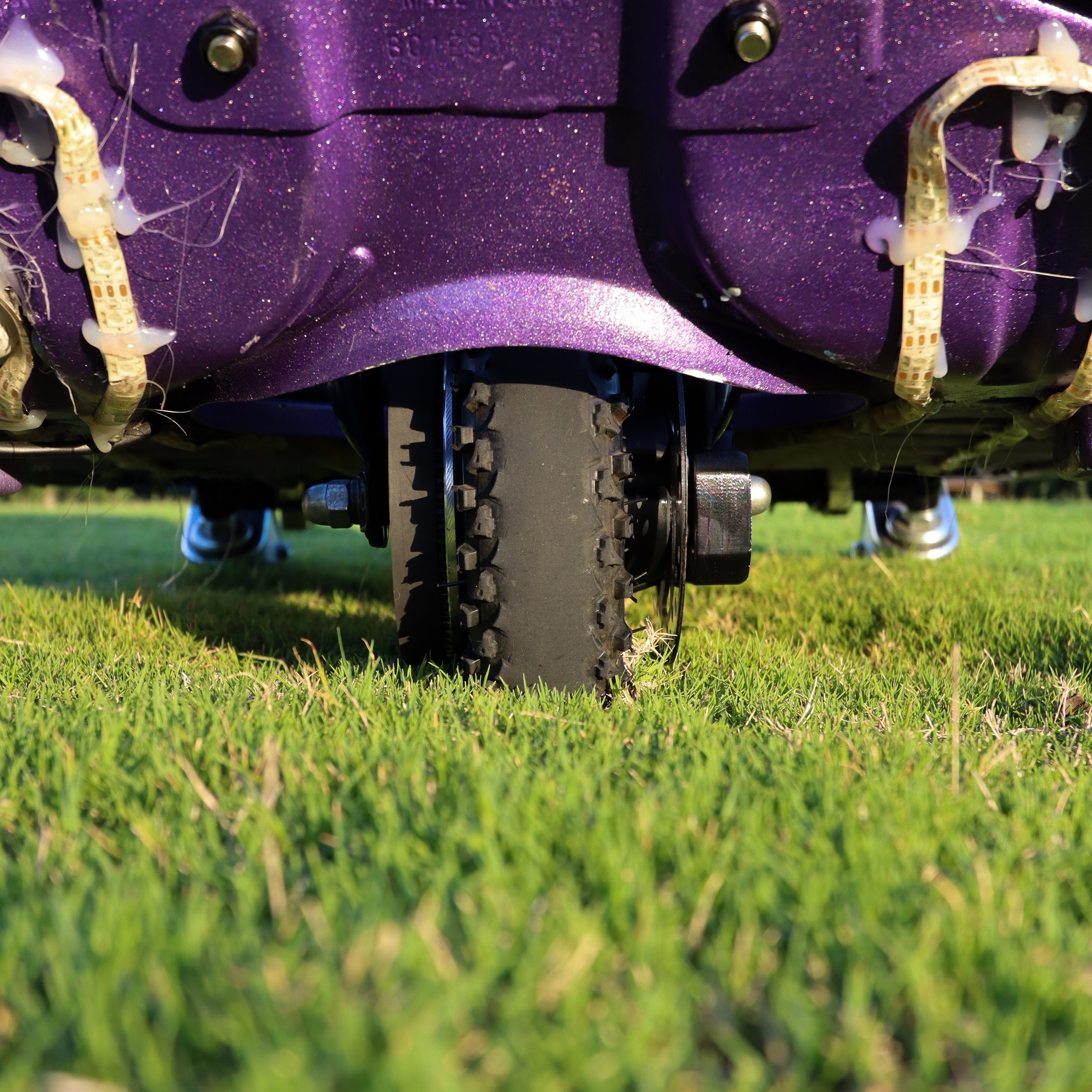 Close-up under the front of a purple crazy cart and front tire on grass.
